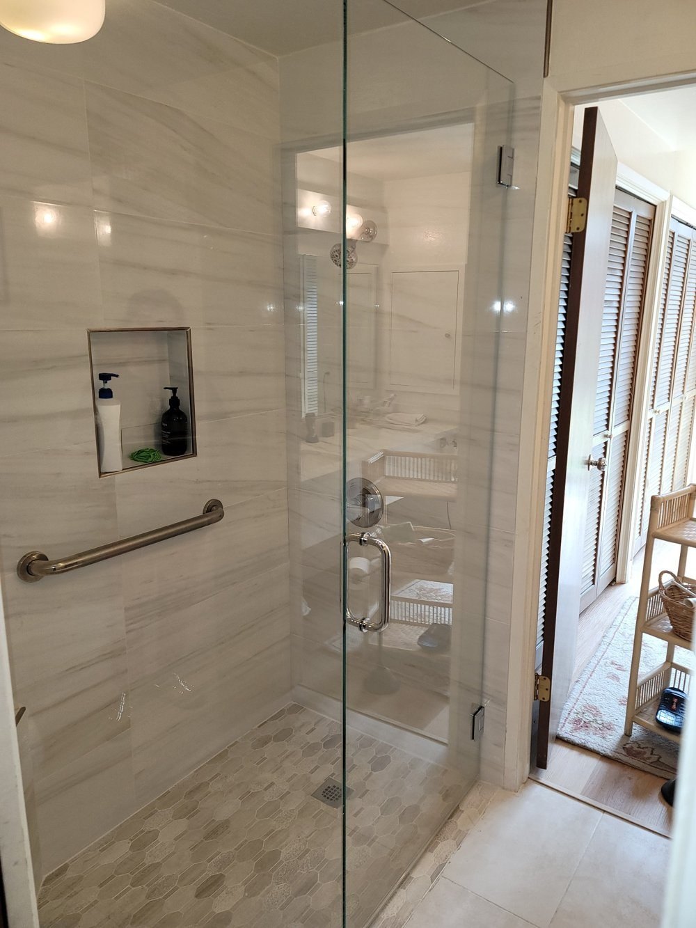 Frameless glass door on a curbless shower with a mosaic tile floor and bathroom beyond