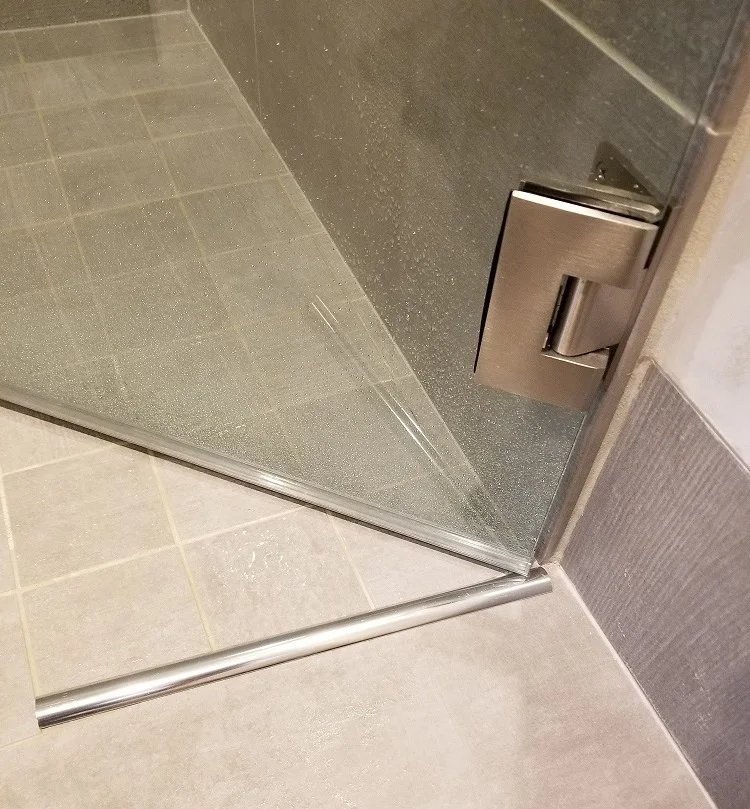 Metal water dam bar on the floor at the bottom of a frameless glass door in a curbless shower