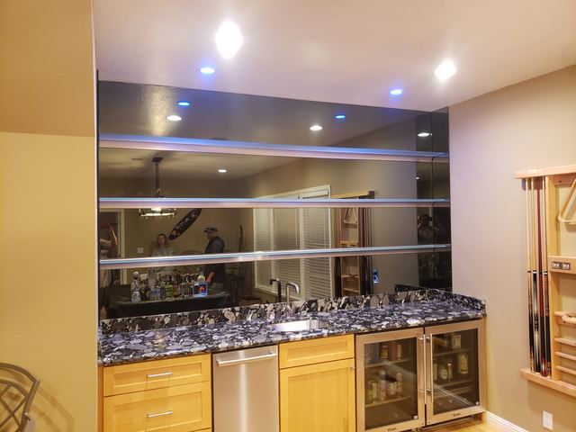 Wall-to-wall bar mirror with glass shelves above a granite counter