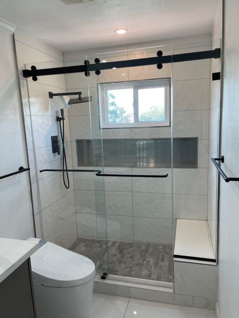 Sliding glass shower door with black rail, tiled bench, long niche and window