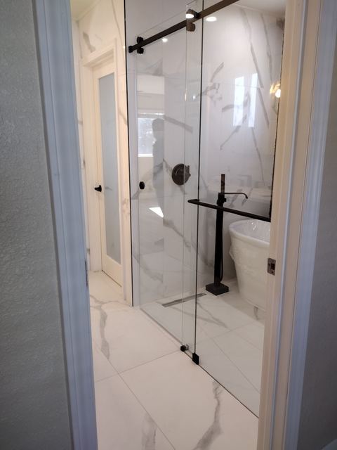 Sliding glass shower door with black hardware in a marble-look bath with a freestanding tub