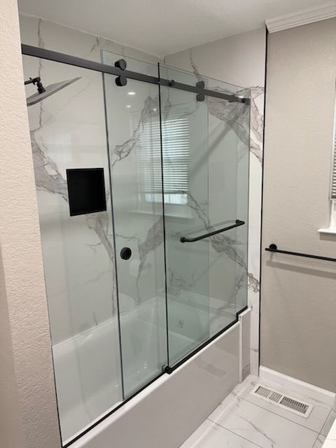 Frameless sliding glass tub enclosure with black rail and hardware in a marble-look tile bath