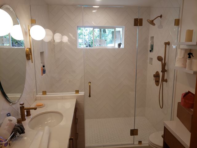Frameless shower door and panel with brass hardware in a herringbone tile shower