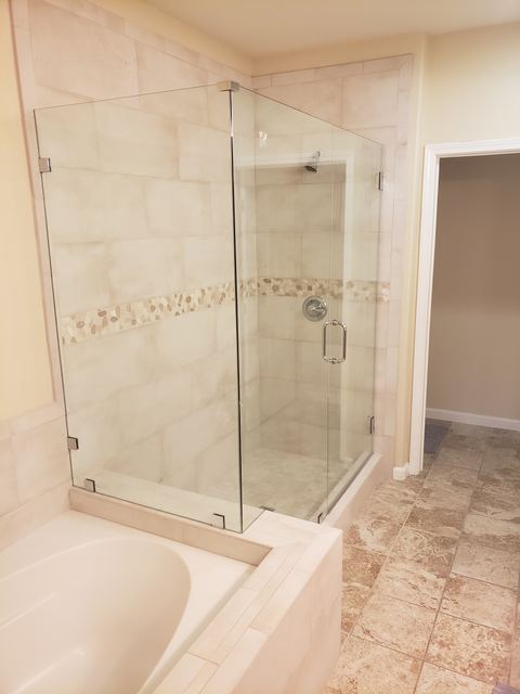 Frameless corner shower enclosure with a pebble accent band over a built-in tub