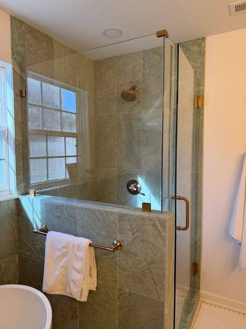 Frameless corner shower enclosure with wall-hinged glass door and Euro Gold hardware in green stone-look tile