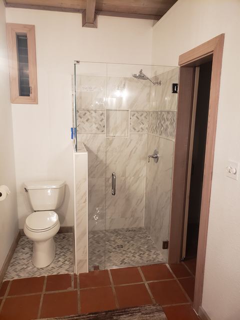 Frameless shower door and panel set on a half wall in a marble-look tile shower
