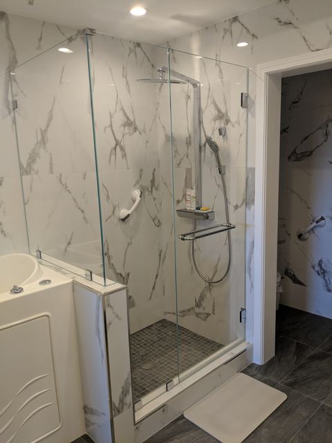 Frameless hinged shower door and panel in a marble-look tile shower
