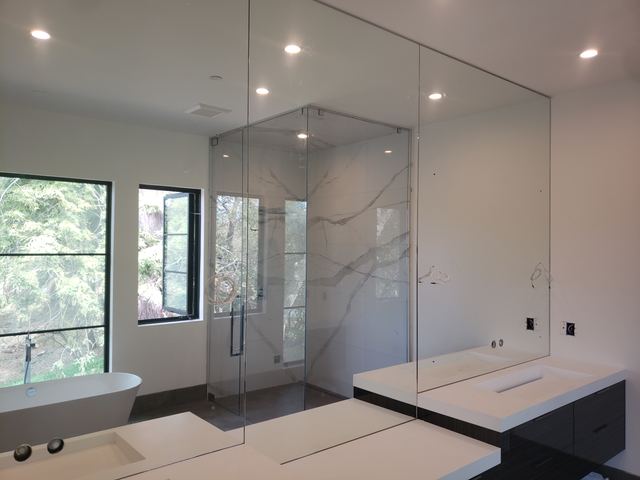 Large vanity mirror with cutouts for wall lighting beside a glass shower enclosure