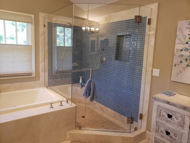 Frameless neo-angle shower enclosure with hinged door and blue glass mosaic tile beside a soaking tub