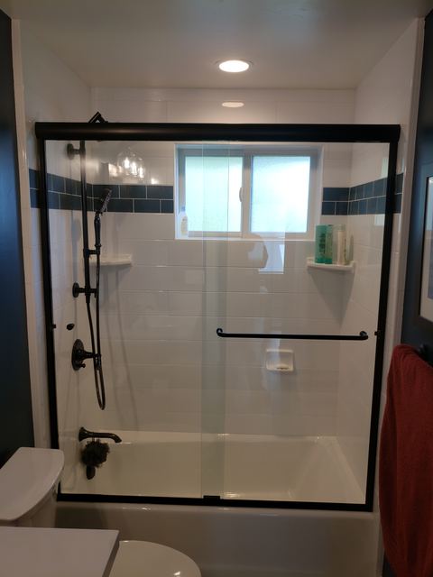 Semi-frameless sliding glass shower door over a tub with black hardware