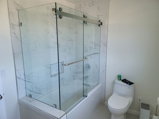 Frameless sliding tub enclosure with fixed return panels in marble-look tile