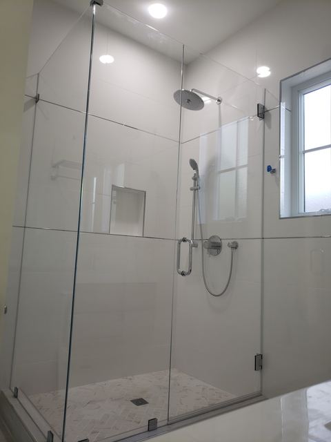 Tall frameless shower enclosure with glass transom panels beside a window