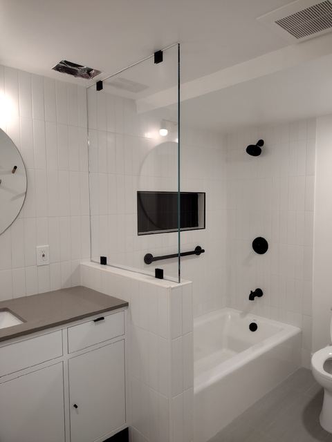Fixed glass splash panel on a tub half wall mounted with black standoff clamps and vertical white tile