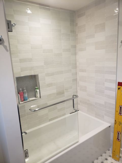 Frameless glass tub panel with chrome towel bar over a white tub