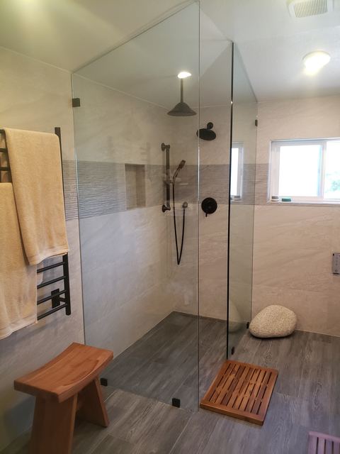 Frameless walk-in shower glass panel with teak bench and black fixtures